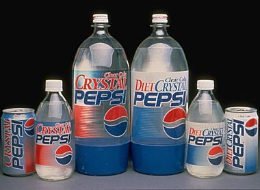 Foto da Crystal Pepsi. Os produtos estão enfileirados horizontalmente com  duas latinhas, duas garrafas de 300ml e duas garrafas de 2l, sendo um de cada da versão normal e um da Diet. A bebida, assim como as garrafas e são transparentes. O rótulo é composto pelo logo da pepsi e as palavras "Clear Cola Crystal Pepsi"